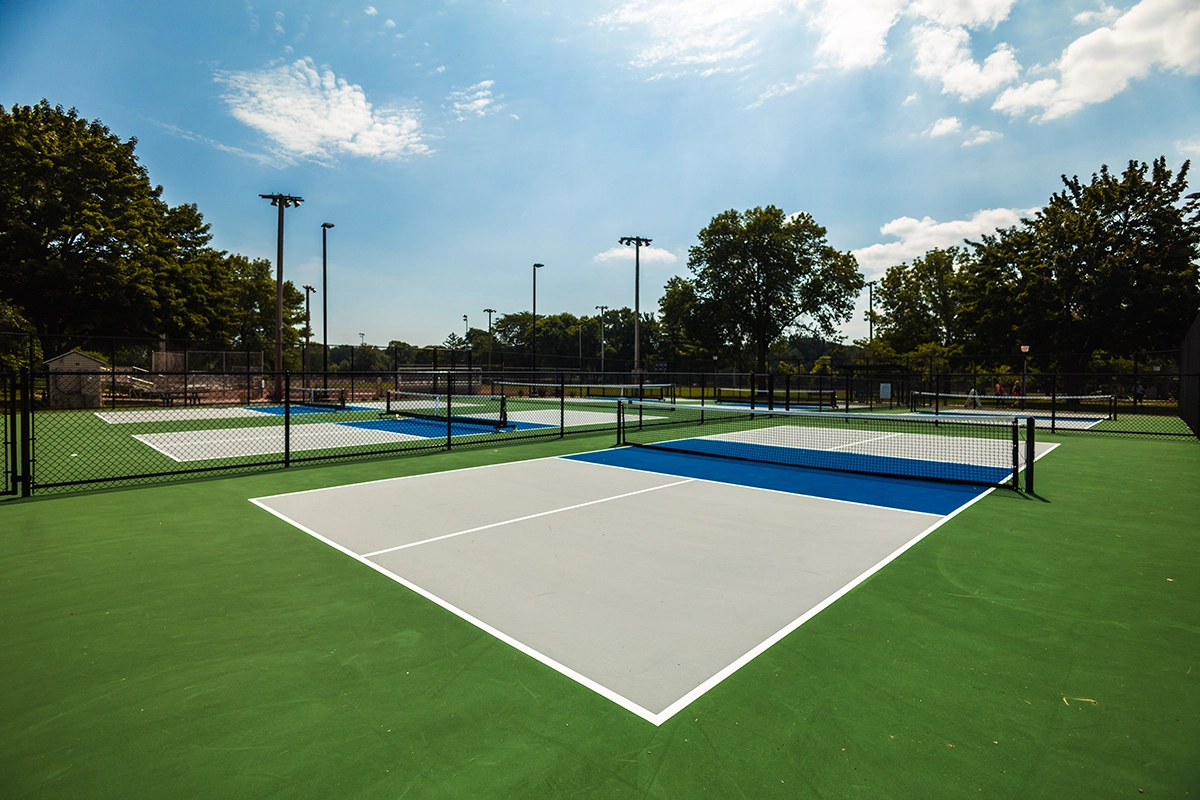 Outdoor pickleball courts with green and blue surfaces, white lines, black fencing, and overhead lighting.